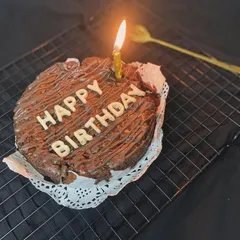 Our brownie cake is perfect for birthdays too! Here it is, complete with a "Happy Birthday" message and a lit candle, ready for a celebration.