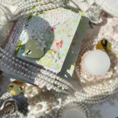 A close-up of the intricate details from the Bridgerton theme, including custom stationery with lace and heart-shaped locks, surrounded by pearls and candles.