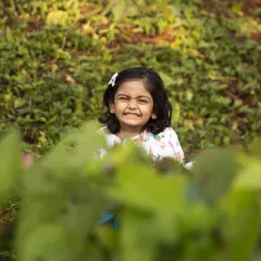 A playful game of peek-a-boo among the green bushes. This image showcases the fun and interactive nature of my kids' photography sessions, capturing a cheeky smile and sparkling eyes.