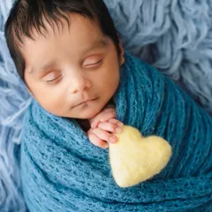 A beautifully styled final shot featuring a newborn swaddled in blue with a small yellow heart prop, demonstrating simple yet effective use of color and texture.