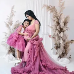 A touching family portrait with an older sister hugging her mother's pregnant belly. Both are in matching pink ruffled gowns, creating a sweet and cohesive look.