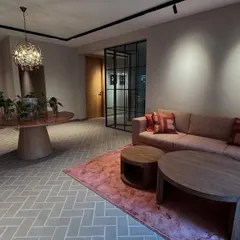 We used earthy and soft tones to design this modern office reception area. The space is lit with a combination of track lighting and a decorative chandelier, creating layers of light. The herringbone floor pattern adds visual interest and leads guests into the main workspace.