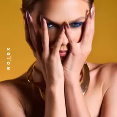 The cover for Roidx Magazine, capturing the 'unstoppable pace of modern femininity'. The intense gaze and bold blue eyeliner are highlighted by a focused lighting setup against a vibrant yellow backdrop.