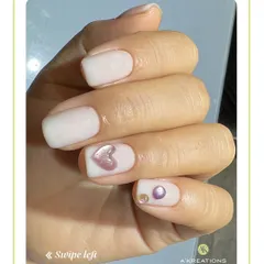 A chic and minimalist design on short nails, featuring a soft white base with a raised 3D heart accent and delicate pearl and gem placements.
