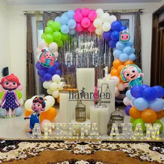 This Cocomelon setup is perfect for a home celebration. It features a colorful balloon arch against a silver fringe curtain, large character standees, and light-up marquee letters for the name.