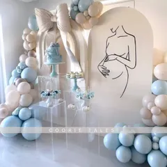 A modern and minimalist baby shower design. This elegant setup features a clean line-art illustration of a mother-to-be, clear acrylic dessert stands, and a soft blue and beige balloon arch for a truly chic celebration.