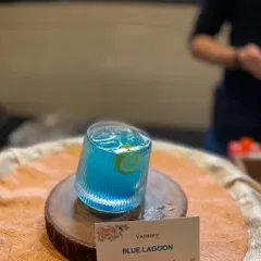 The classic Blue Lagoon mocktail, beautifully presented in a ribbed glass on a wooden platter. A refreshing choice for any party.
