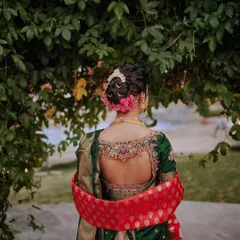 A detailed look at the back of this stunning bridal updo. The neatly tied bun, decorated with pink flowers, is a timeless choice that showcases the bride's jewelry and outfit beautifully.