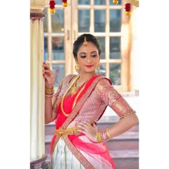A beautiful moment captured in a custom half-saree lehenga. The outfit features a pink and silver blouse with intricate embroidery, paired with a white and red skirt, perfect for traditional ceremonies.