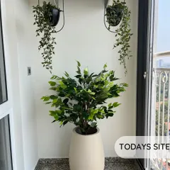 A beautiful balcony setup using only artificial plants. A large Ficus tree in a cream planter is complemented by hanging creepers for a lush, maintenance-free look.