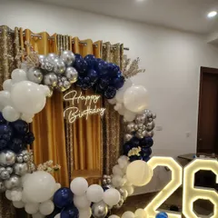 This 26th birthday decoration features a modern color scheme of navy blue, white, and silver. The balloon ring is set against a gold curtain for extra glamour.