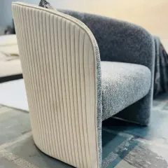 A detail shot of a modern armchair, showing the contrast between the textured grey fabric and the vertically stitched cream leather on the back. This highlights our focus on combining materials for a unique finish.