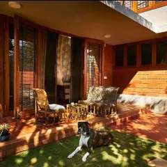 This covered patio at the Reshma House is an extension of the living space, defined by its exposed brick walls and terracotta floor tiles. It’s a perfect example of creating a seamless transition between indoor and outdoor living.