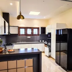 This open-concept modular kitchen is designed for both style and efficiency. It features a sleek two-tone design with high-gloss white and dark wood finish cabinets, a functional island counter, and integrated appliances, all illuminated by a combination of recessed lights and a statement pendant lamp.