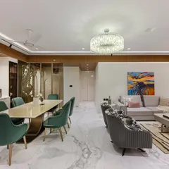 An open-plan living and dining space in a South Mumbai home, featuring a fluted ceiling border and pastel sofas with intricate detailing. The dining area stuns with an exotic marble wall, creating a captivating focal point for upscale gatherings.