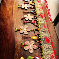 This side angle of the 'Taana Baana' toran highlights the texture and layers. From the embroidered lace to the wooden flowers and mirror garlands, it's a feast for the eyes.