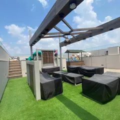 This expansive rooftop lounge in Gurugram is covered with durable artificial grass, creating a comfortable and stylish setting for outdoor furniture under a modern pergola.