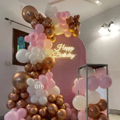 A chic 'Happy Birthday' decoration in pink, white, and bronze. The arched backdrop and balloon garland can be customized in any color to match your party's theme.