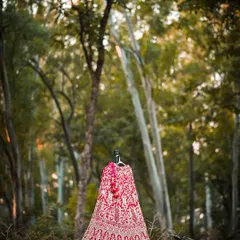 An artistic shot of the bridal lehenga displayed on a mannequin in a forest, contrasting the rich fabric with the natural environment.