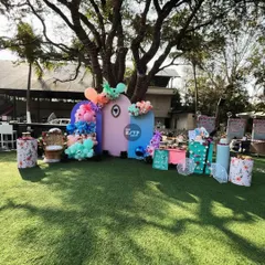 For this outdoor baby shower, we created a fun and colorful backdrop on a lush green lawn. The setup features abstract pastel panels, vibrant balloon clusters, and a dedicated dessert table, all centered around a large tree for a playful, natural feel.