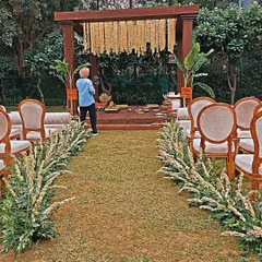 An aisle view of an outdoor puja setup. I lined the walkway with fresh tuberose arrangements, leading the eye towards the wooden mandap decorated with traditional marigold strings and banana plants.