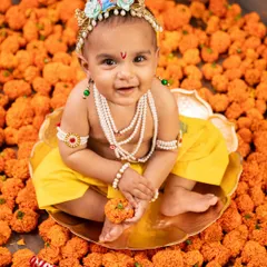 A smiling little Krishna sitting in a bed of marigolds. The bright orange flowers and his happy expression make this a wonderfully joyful shot.