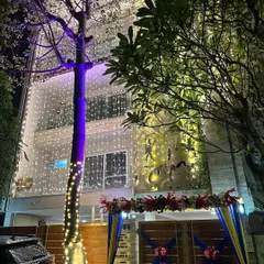 A full view of a wedding house at night. The entire building is lit up with fairy lights, and the entrance gate is decorated with colorful drapes and flowers.