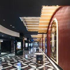 The main corridor at INOX Jalosa is a dynamic and glamorous passage. The design uses a bold, geometric floor pattern, reflective surfaces, and arched doorways with integrated lighting to guide patrons and build a sense of cinematic drama. The deep red leather-clad walls add a touch of classic theater opulence.