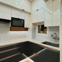 A close-up of a dual-tone L-shaped kitchen. The high-gloss white upper cabinets make the space feel bright, while the dark grey lower cabinets ground the design. The under-cabinet lighting highlights the beautiful marble-patterned backsplash.