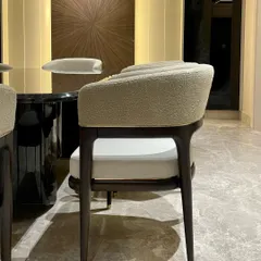A detail shot of our luxurious dining chair, featuring an ebony-stained solid wood frame, sleek metal accents, and a comfortable bouclé fabric seat. The curved back provides both support and style.