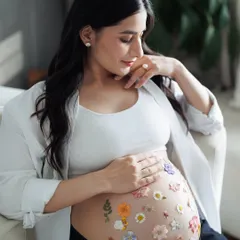 A quiet moment of reflection for the mother-to-be. Seated comfortably, she looks down at her flower-adorned belly with a gentle smile. It's a little bit of magic.