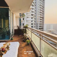 A beautiful city view from a well-appointed balcony at sunset. The space is simply decorated with potted plants and a small seating area to maximize the sense of openness.
