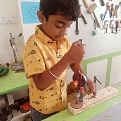 A student carefully operates a hand drill. We start with manual tools to build a strong foundation and understanding of mechanics before moving to power tools.
