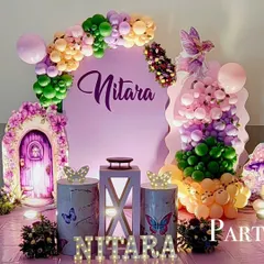 A whimsical fairy theme party with a magical door prop. The purple backdrop is complemented by colorful balloon arrangements, butterfly-themed pedestals, and light-up marquee letters.