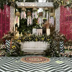 A stunning boho-themed Mehendi stage. The design features a chevron-patterned floor, a backdrop of rustic screens, and lush arrangements of pampas grass, sunflowers, and roses.