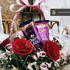 A charming and sweet gift basket perfect for any occasion. This arrangement features rich red roses and two bars of Cadbury Dairy Milk chocolate, all tied together with a beautiful pink ribbon.