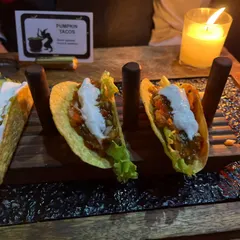 'Pumpkin Tacos' served on a rustic wooden stand. This dish perfectly captures the essence of Halloween, combining a seasonal flavor with a crowd-pleasing format.