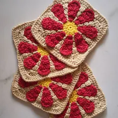 These are the individual granny squares that form the foundation of my Groovy Daisy bag. Each square is carefully stitched with a bright yellow center and red petals, ready to be joined into a beautiful and functional accessory.