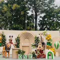 A wide shot of Avyaan's Mickey Mouse safari party. This setup combines the adventure of a safari with the fun of a beloved character, featuring a neutral-toned backdrop, jungle foliage, and cutouts of Mickey in his safari gear.