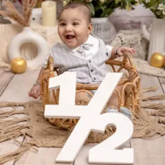 Halfway to one and full of smiles. This little boy celebrates his six-month milestone in a rustic-themed setup, sitting in a wicker chair with a "1/2" sign to mark the special occasion.