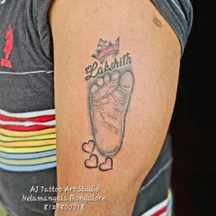 A precious memory made permanent. This tattoo features a baby's footprint, name, and a small crown, a perfect tribute for a new parent on their upper arm.