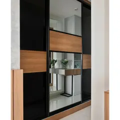 A custom Aristo sliding wardrobe featuring a bold combination of black lacquered glass, wood-finish laminate, and a central mirror panel. This design adds functionality and makes the room feel more spacious.
