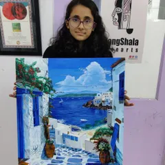 A proud student displays her finished acrylic on canvas painting of a Santorini landscape. This shows the complete journey from a blank canvas to a vibrant, portfolio-worthy artwork.