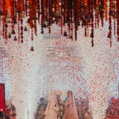 A shower of rose petals rains down on the couple during their varmala exchange. This iconic moment is amplified by dramatic lighting and a backdrop of hanging temple bells, creating a truly divine atmosphere.