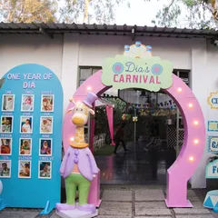 The entrance to Dia's Carnival, featuring a personalized archway, a milestone board celebrating her first year, and a dapper giraffe character to welcome guests.