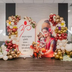 This is a beautiful example of a traditional Godh Bharai or baby shower decoration. The backdrop features a serene illustration of a mother and Ganesha, framed by an elegant balloon arrangement in white, gold, and maroon.