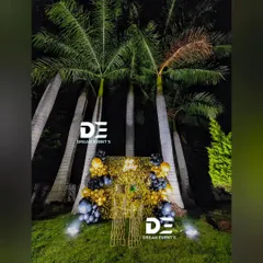 A surprise party setup featuring a gold shimmer wall nestled among palm trees, creating a glamorous and unexpected focal point for an outdoor celebration.