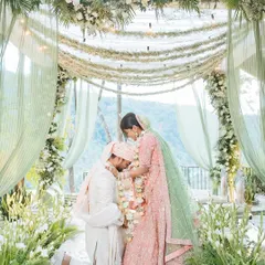 A groom bows down to touch the bride's feet during the varmala ceremony, a modern and respectful gesture of love.