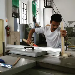 A student gains practical experience on the panel saw, a fundamental machine for accurately sizing wood panels for furniture projects. Safety and precision are the focus of this training.