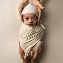 Held safely in parental hands, this little one looks right at the camera. The simple wrap and cap keep the focus on those beautiful, curious eyes.